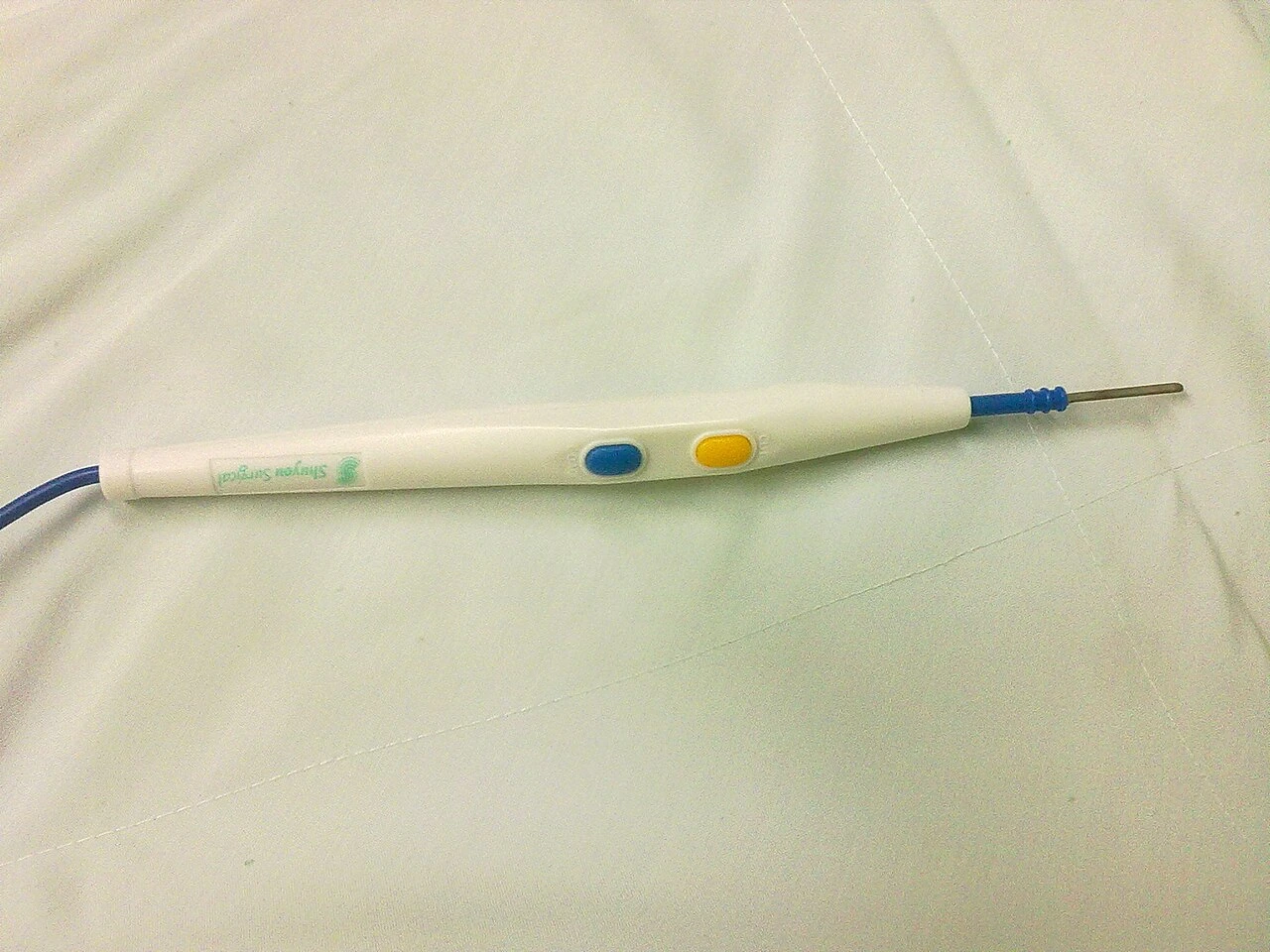A pale insulated handpiece has two colored buttons, a short metal electrode and an attached cable.