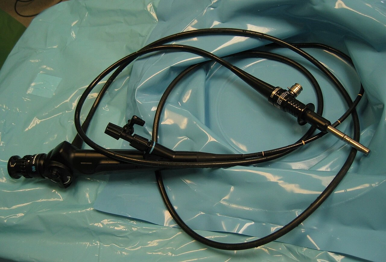 A dark flexible tube with a control body and attached connections rests on a green drape.