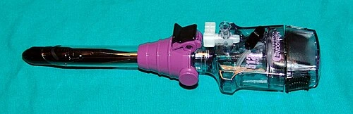 A short dark insertion piece is seated in a transparent cylindrical housing with a colored collar and side port.