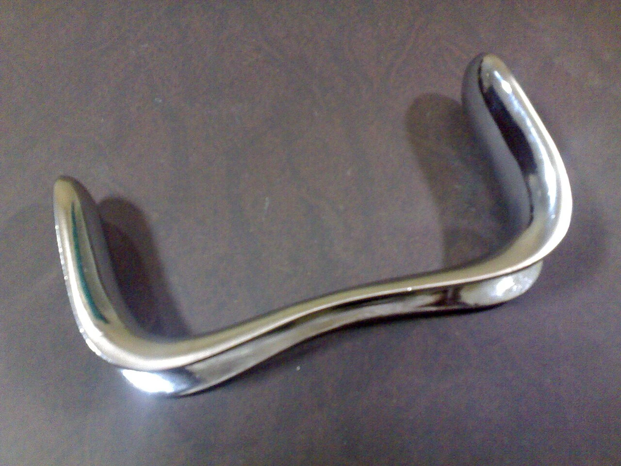 A polished double-ended curved metal tool has broad scoop-shaped blades at opposite ends.
