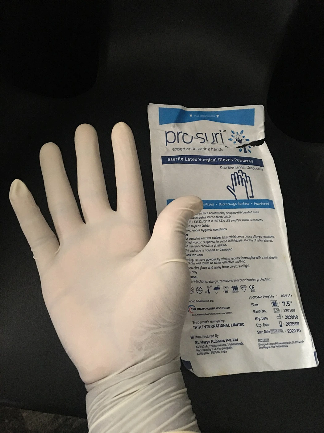 A pale glove with long fingers and a cuff lies beside its individual paper wrapper.